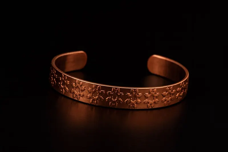 Pulseira de cobre com flores em relevo repetidas, sobre fundo preto